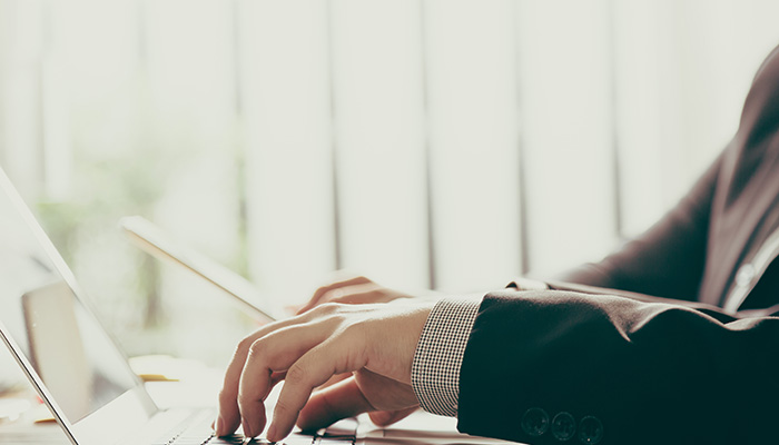 Person in a suit typing on a laptop